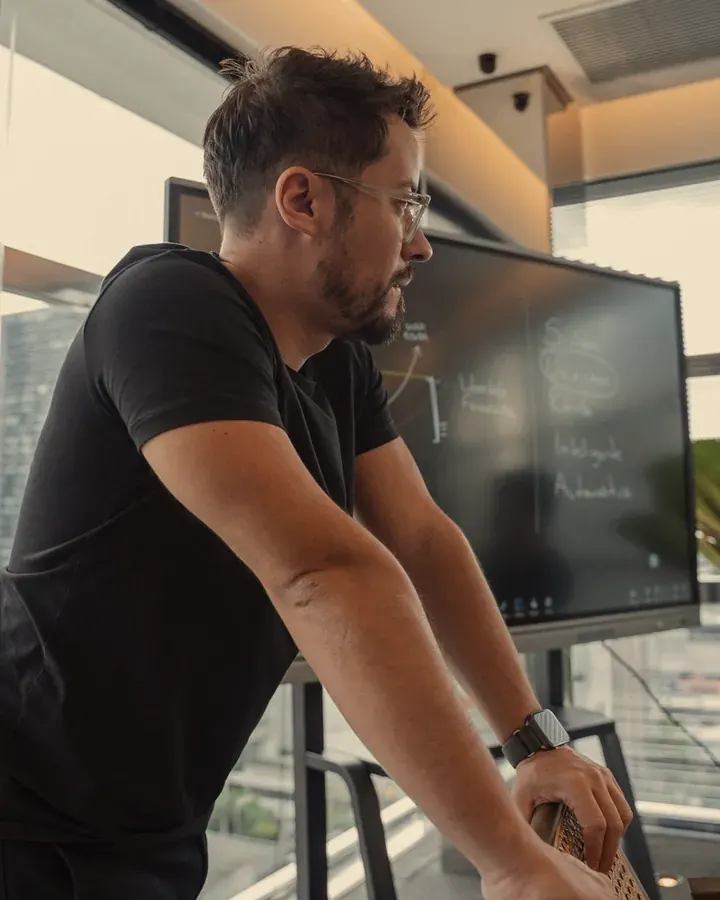 Suriel Ports em pé, de camiseta preta, explicando um conteúdo diante de uma tela